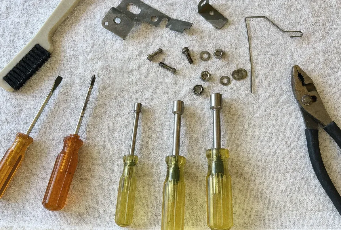 Nut drivers with yellow handles, a screwdriver and loose hardware laid out on a cloth