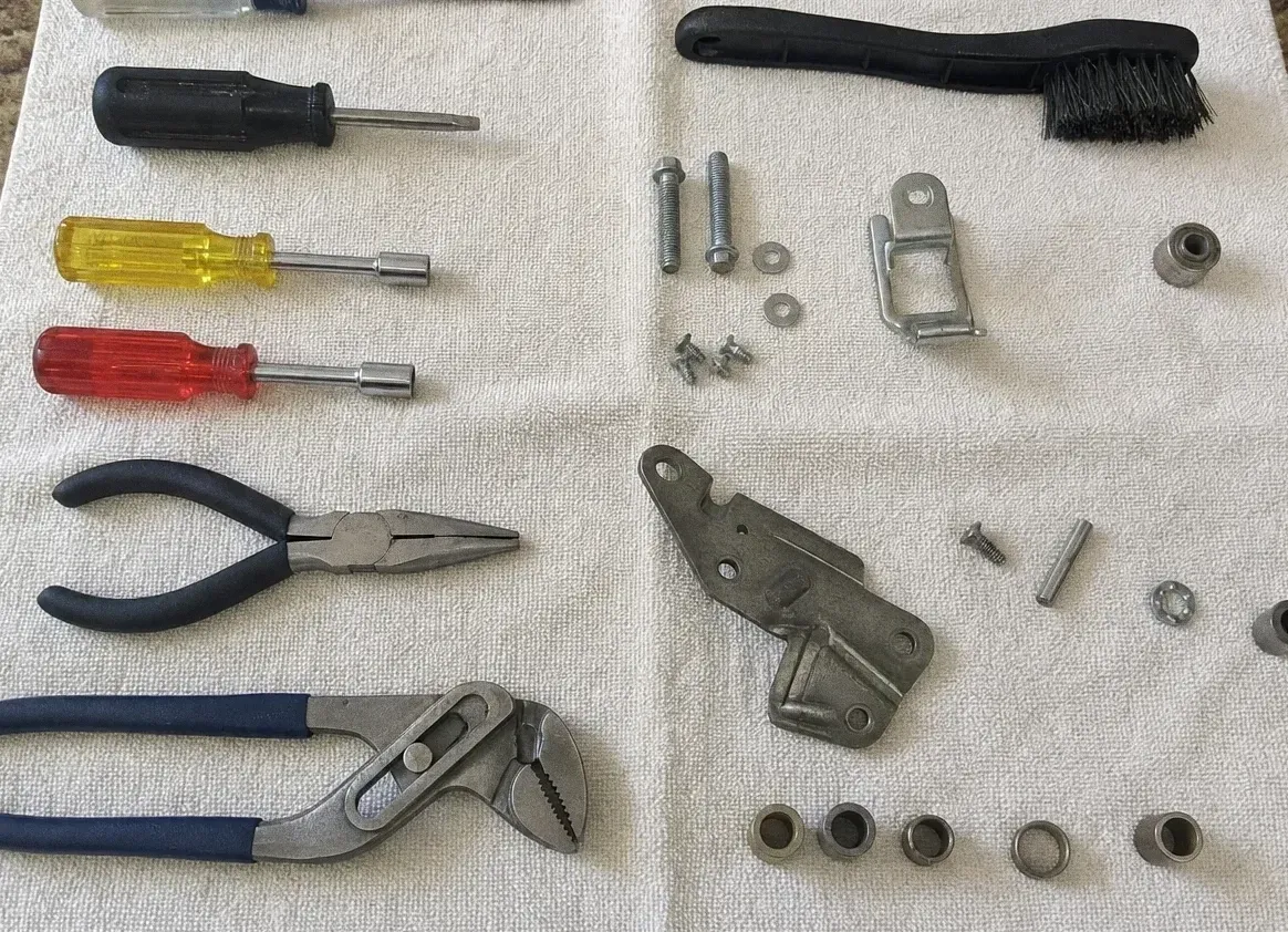 Screwdrivers and pliers beside a metal latch bracket and small washers on a cloth