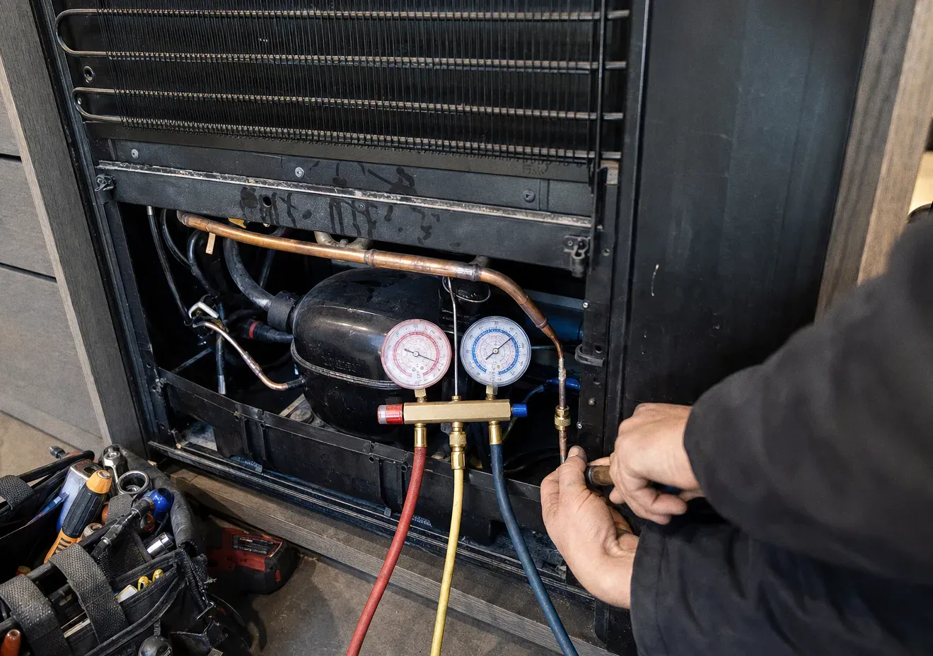 A condenser coil and compressor with manifold gauges attached, hands adjusting a valve