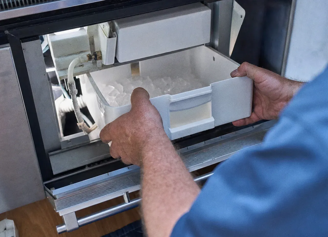 Hands drawing a white ice container out of a freezer drawer